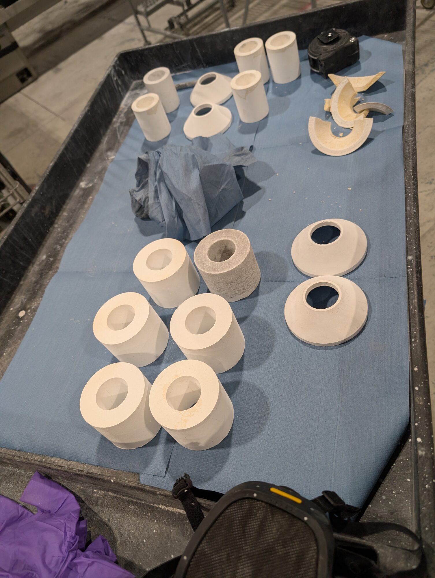 A tray of white cast alumina cylinders and flared cones on blue cloth