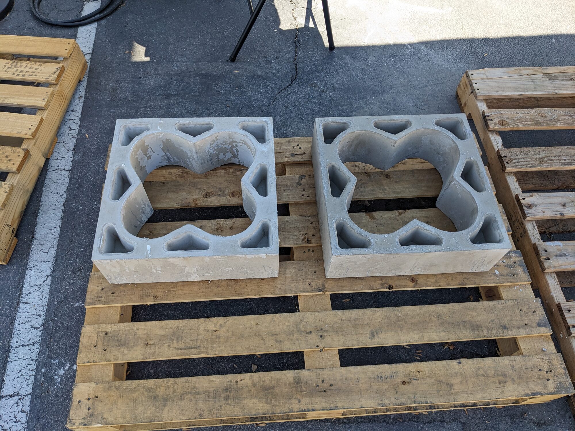 Two finished gray refractory blocks with quatrefoil voids, on a pallet in the yard