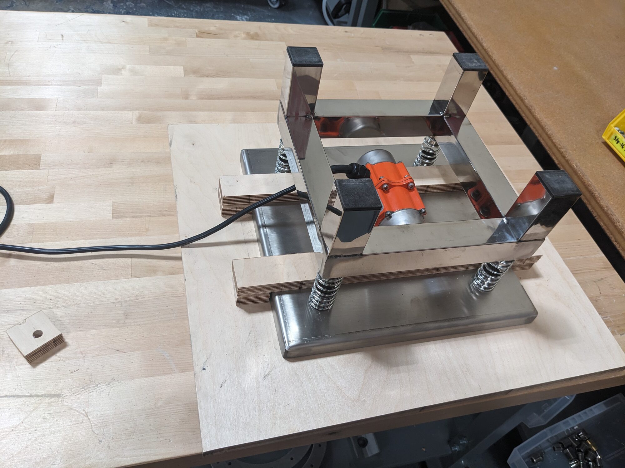 Vibratory platform on plywood with spring mounts, eccentric motor, and catch tray