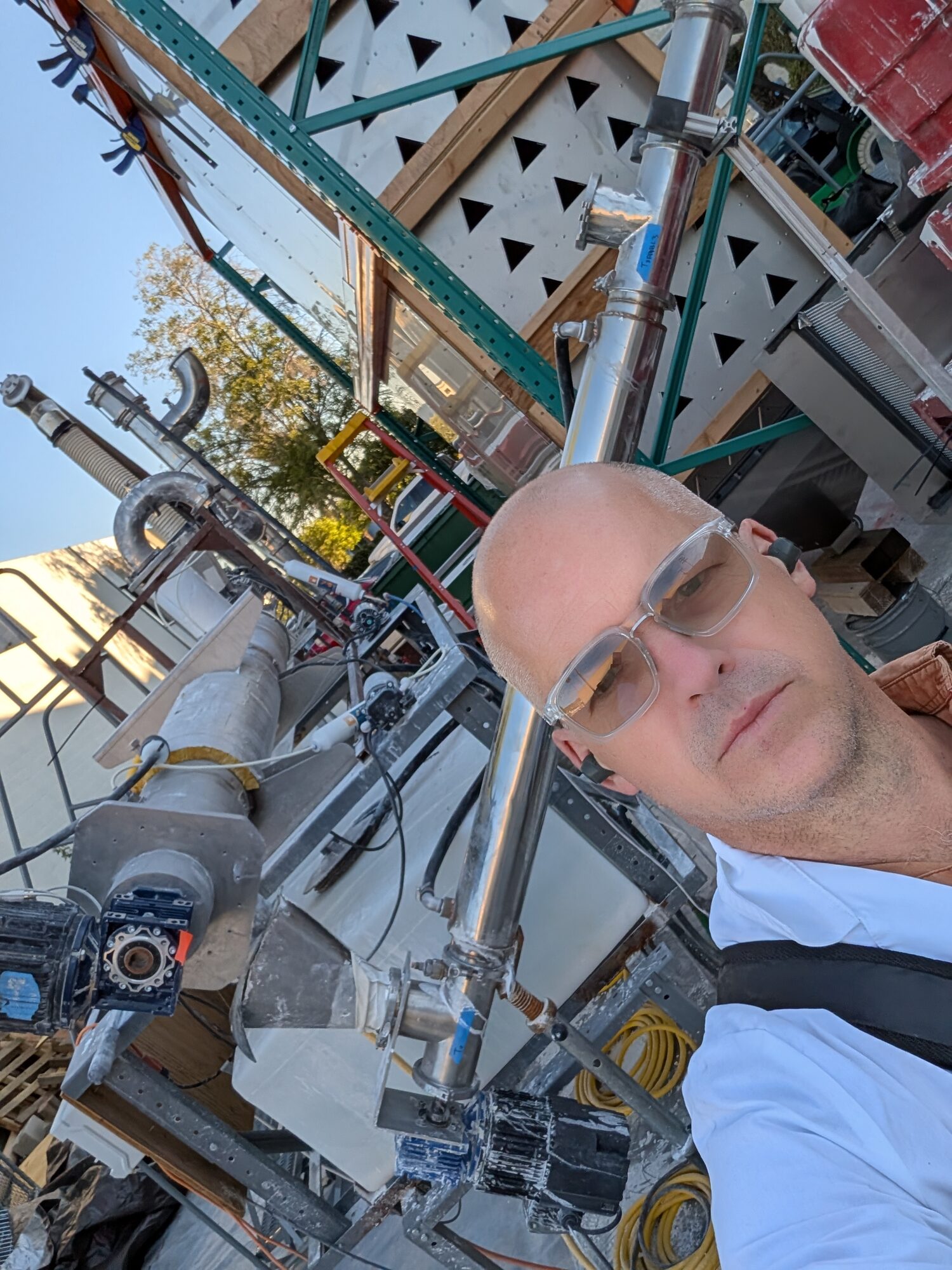 Eghan in safety glasses beside stainless pipework and a geared drive on the prototype build