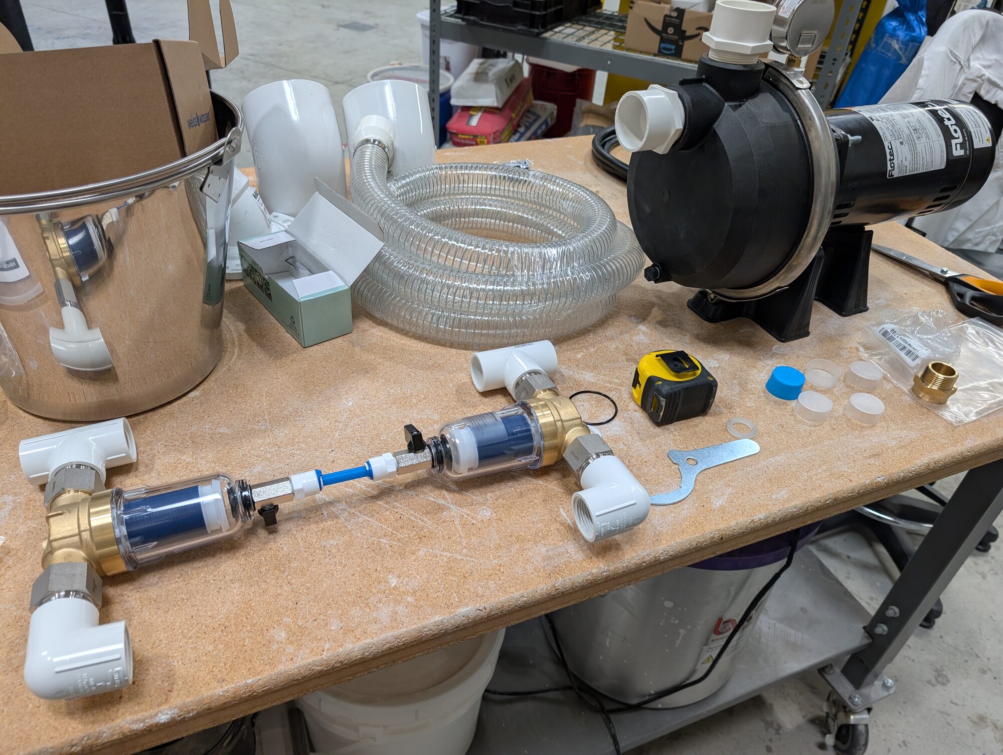 A workbench with the pump, two clear-bowl filter housings joined by fittings, and a coil of clear hose