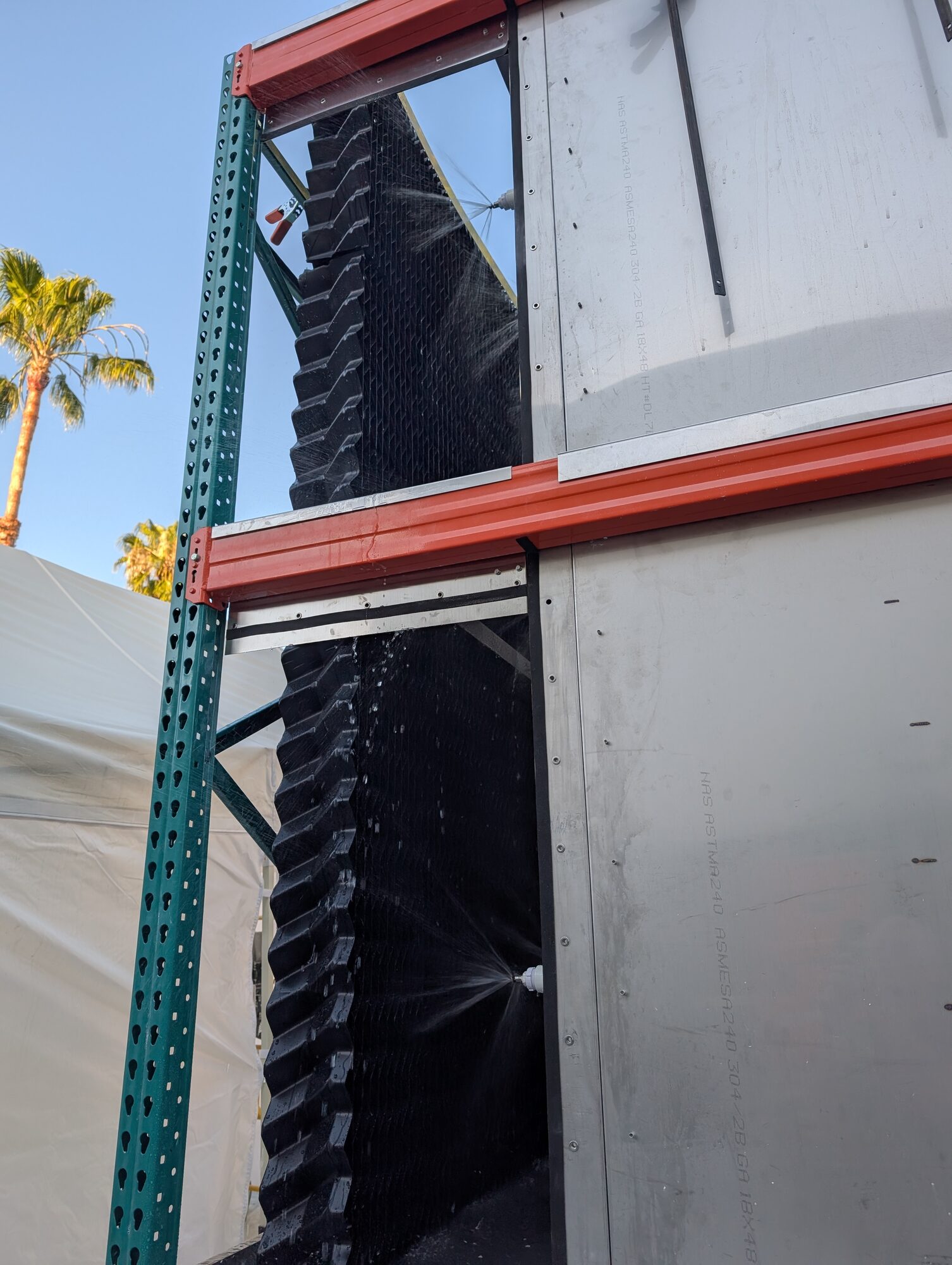 Spiral nozzles misting water onto a tall black media wall on the side of the carbonation skid