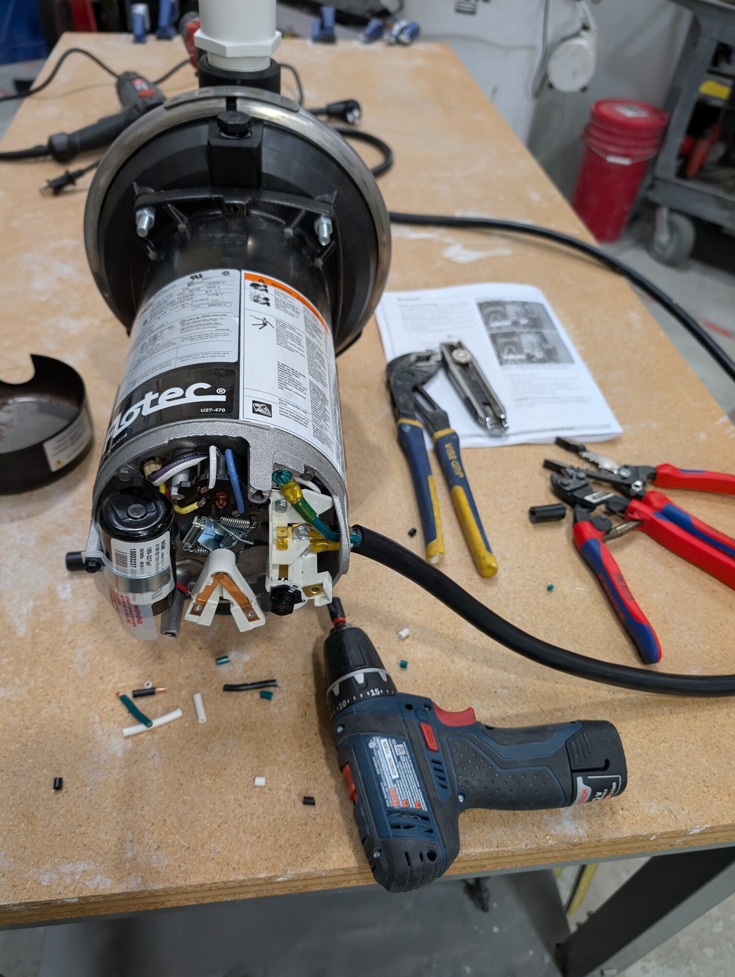 A Flotec pump opened up on the bench with its wiring exposed, tools and the manual alongside