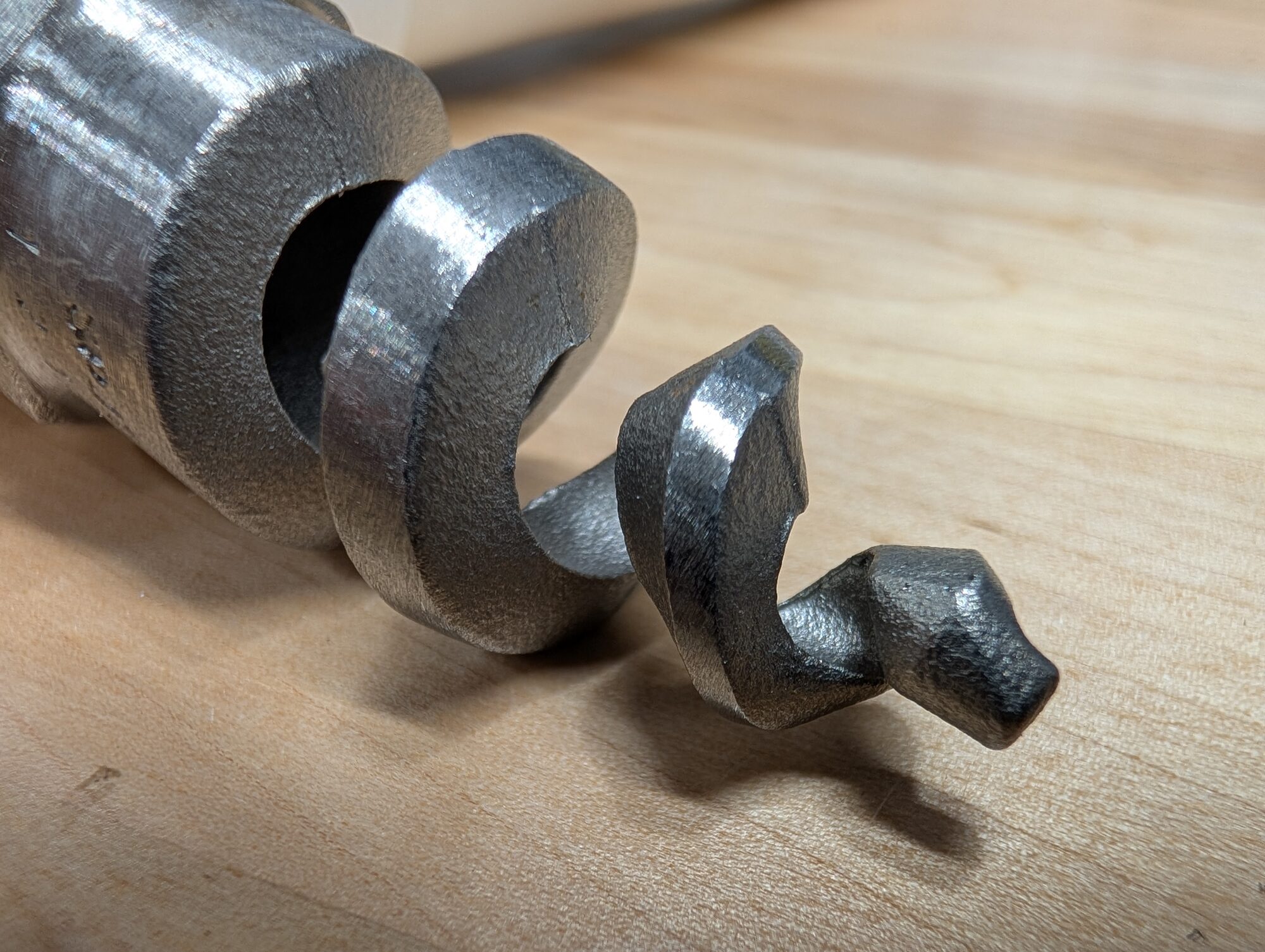 A stainless spiral spray nozzle lying on a wooden bench