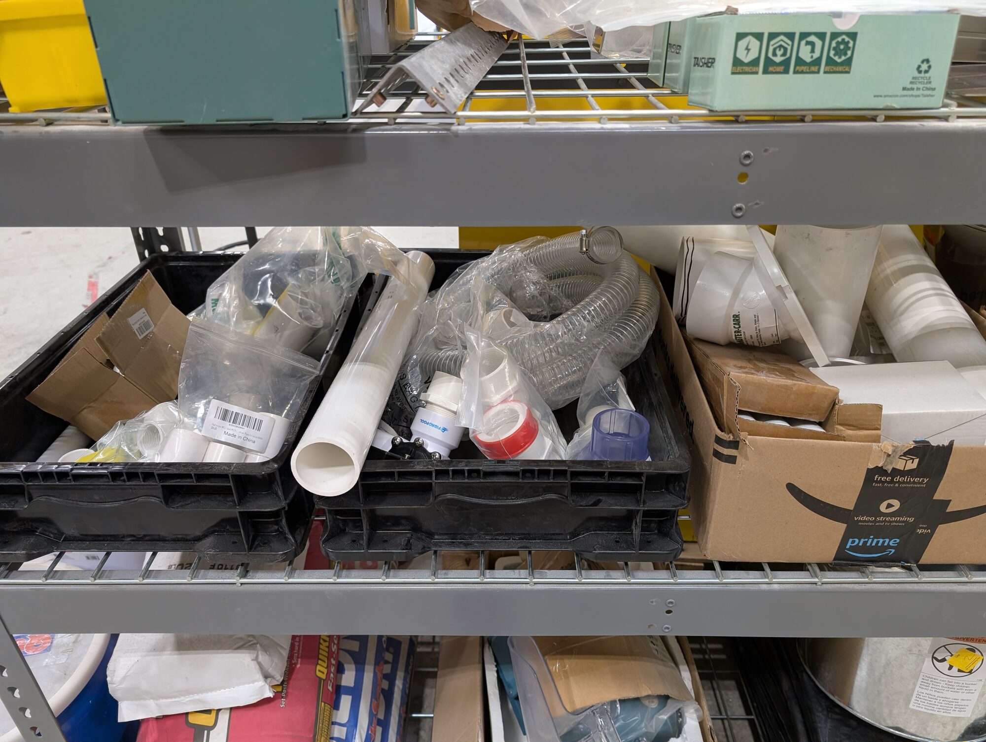 A shop shelf holding bins of PVC fittings, clear suction hose and valves