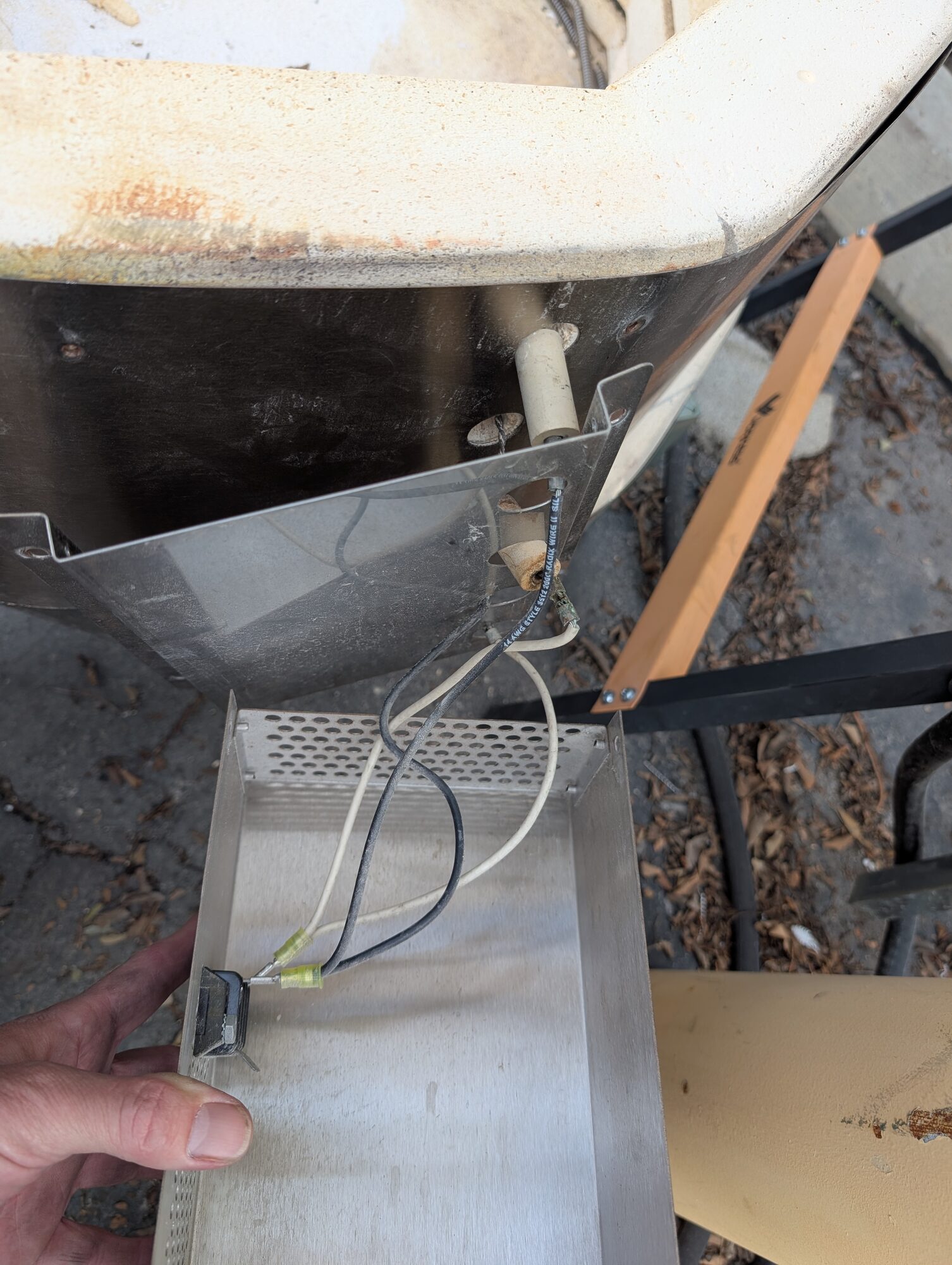 A hand holding a perforated stainless box with a switch, wired up under a beige tank