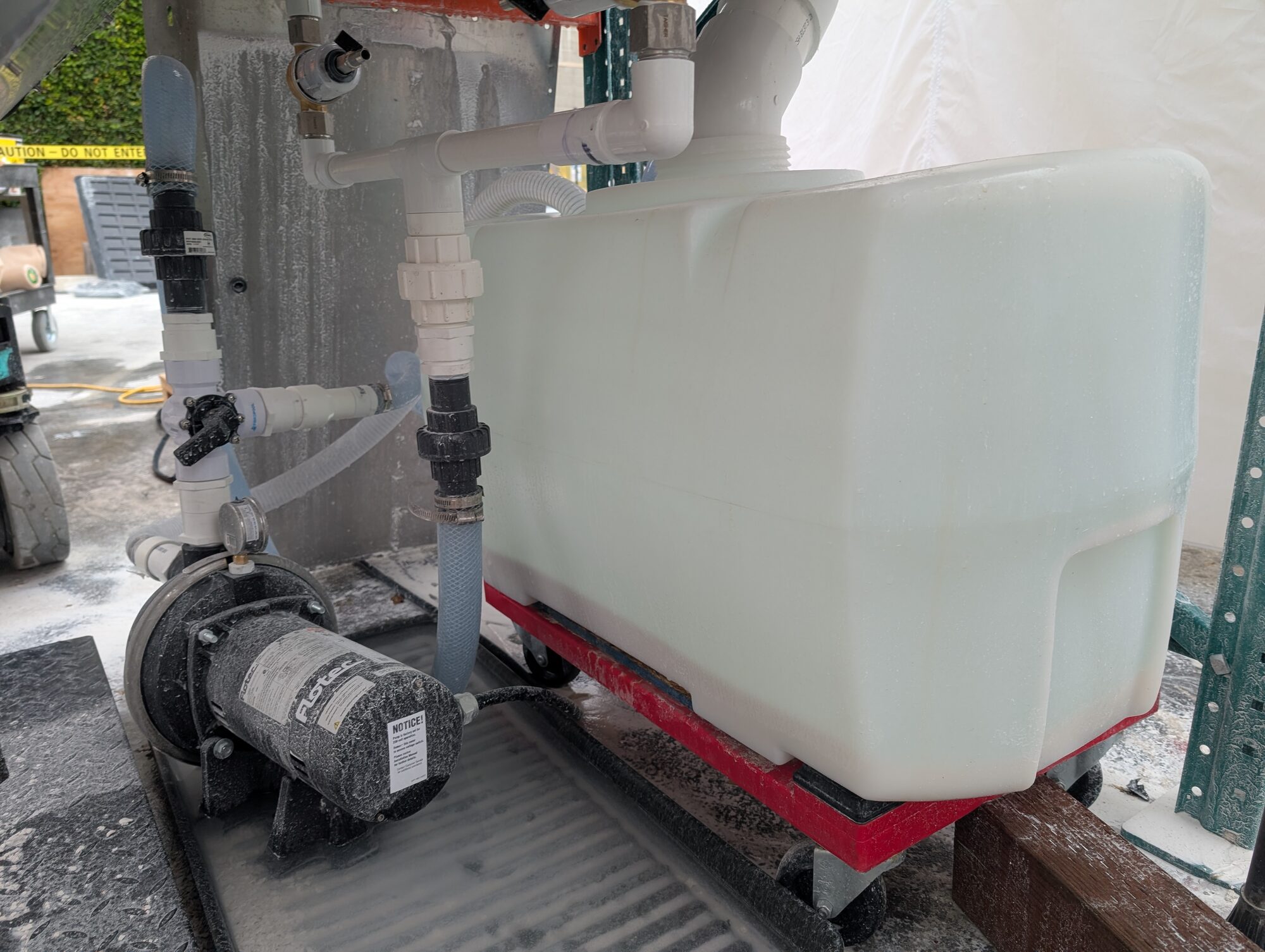 The water tank on a red dolly next to the pump, plumbed into the skid