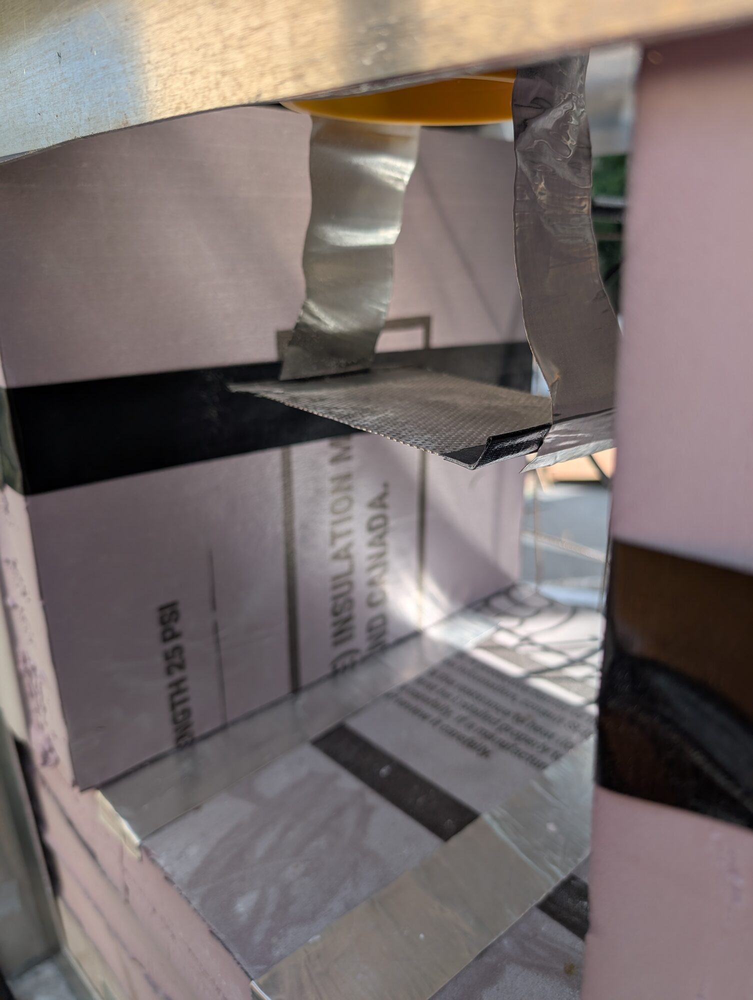 A taped sheet metal baffle inside the foam-lined duct, narrowing the passage under the drop point