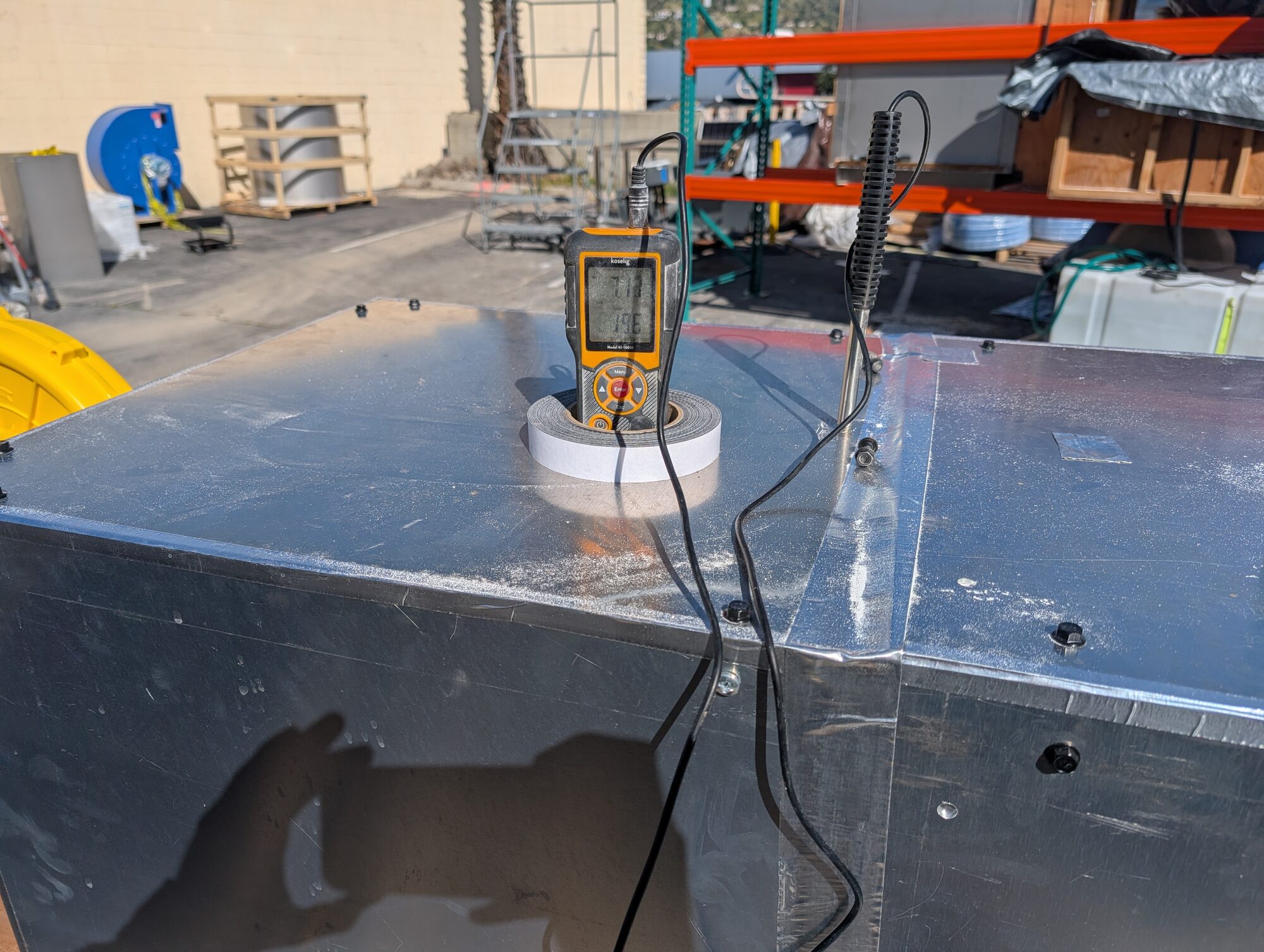 An anemometer sitting on the housing with its probe lead running into the duct