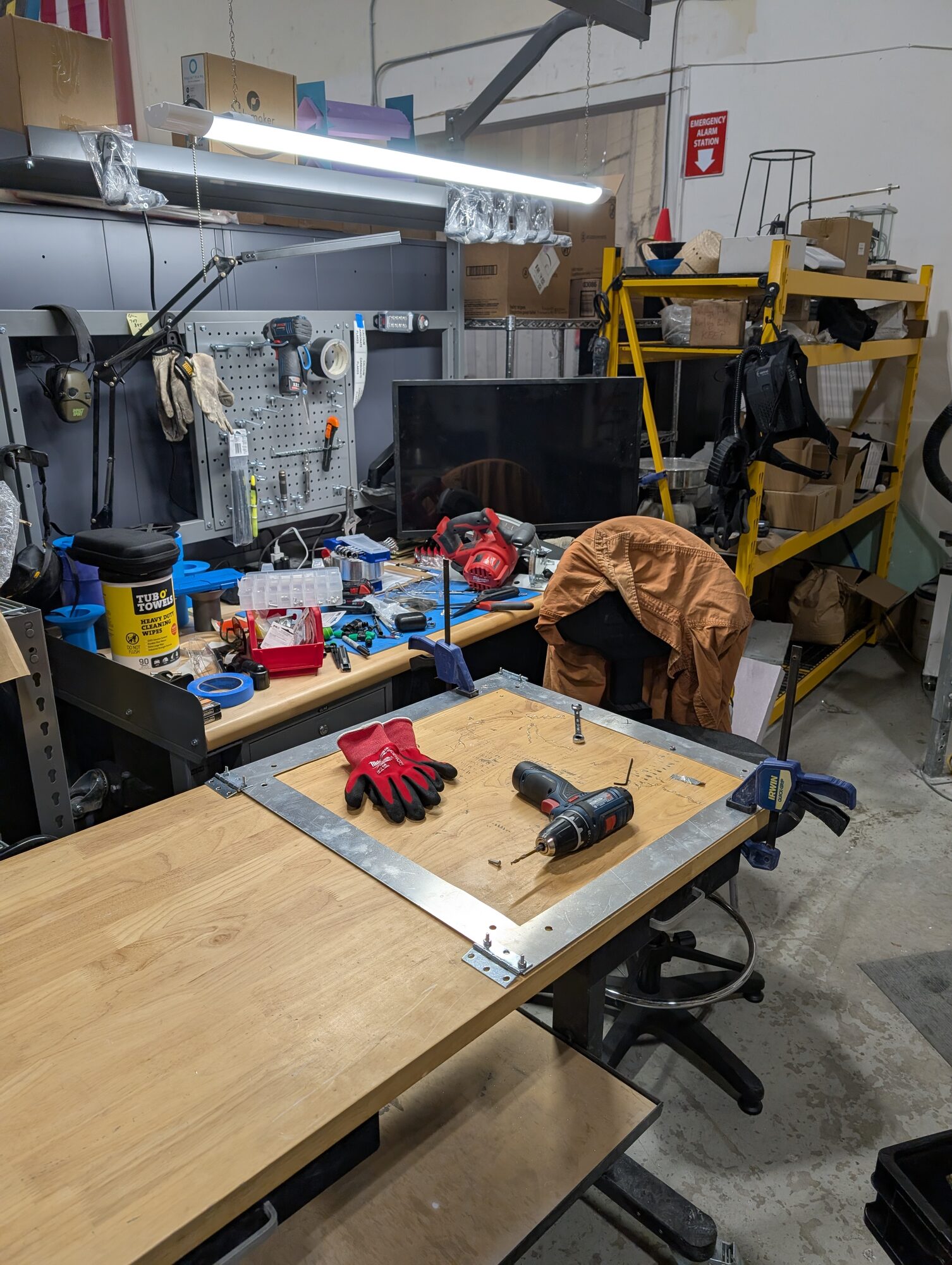 An aluminum panel frame clamped down on the shop bench with a drill and gloves on it