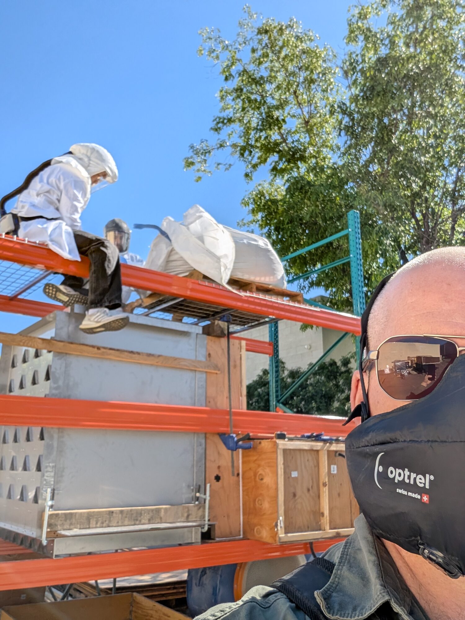Looking up at pallet racking loaded with white sacks on a mesh deck, plywood crates below