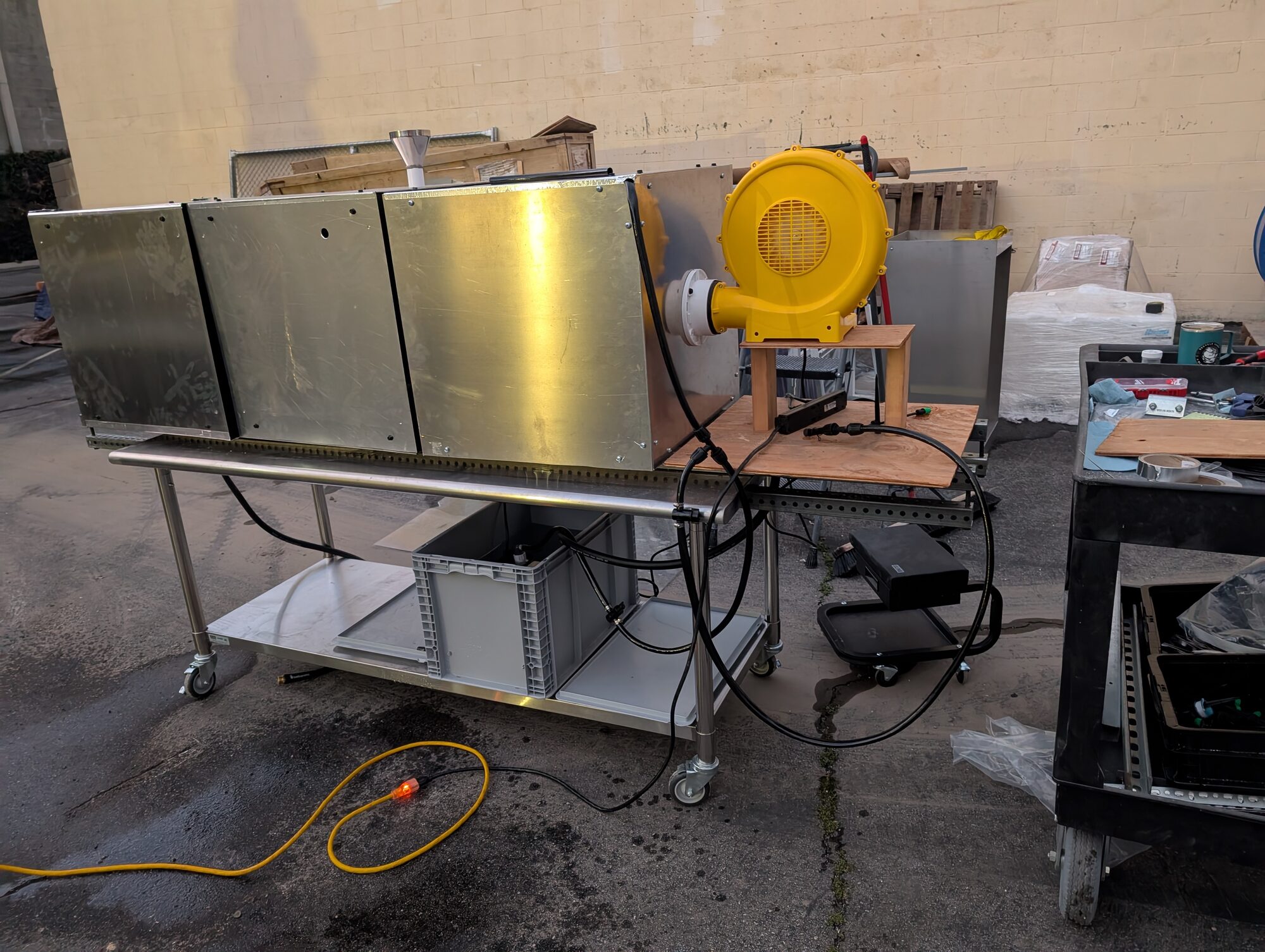 A stainless wheeled table carrying three aluminum cubes in a line with a yellow blower at one end